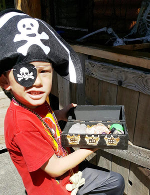 young boy wearing pirate hat and patch holding up a treasure chest full of pirate treasures